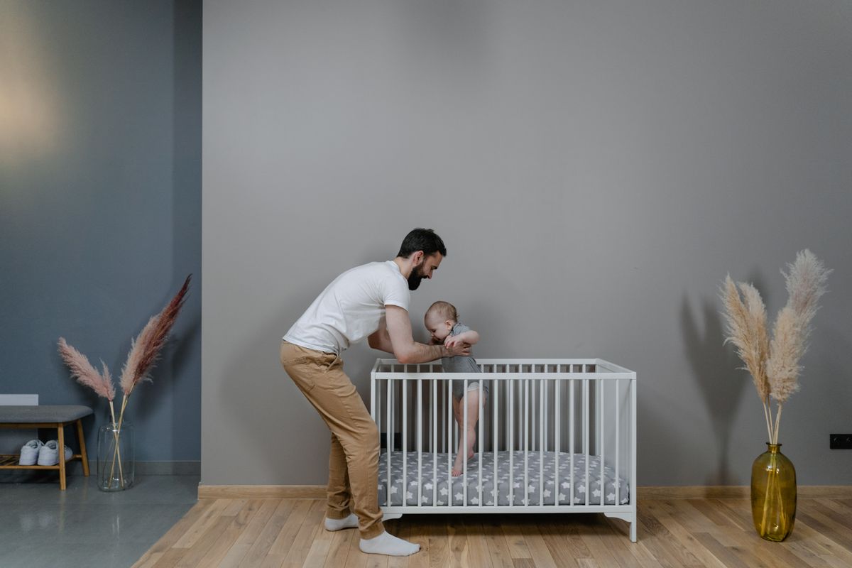 A father lifting his baby out of a white crib in a calm, minimal nursery