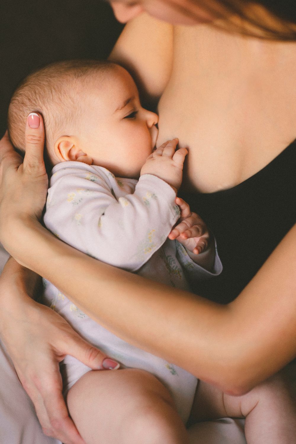 A mother breastfeeding her newborn in soft evening light during an evening cluster feeding session