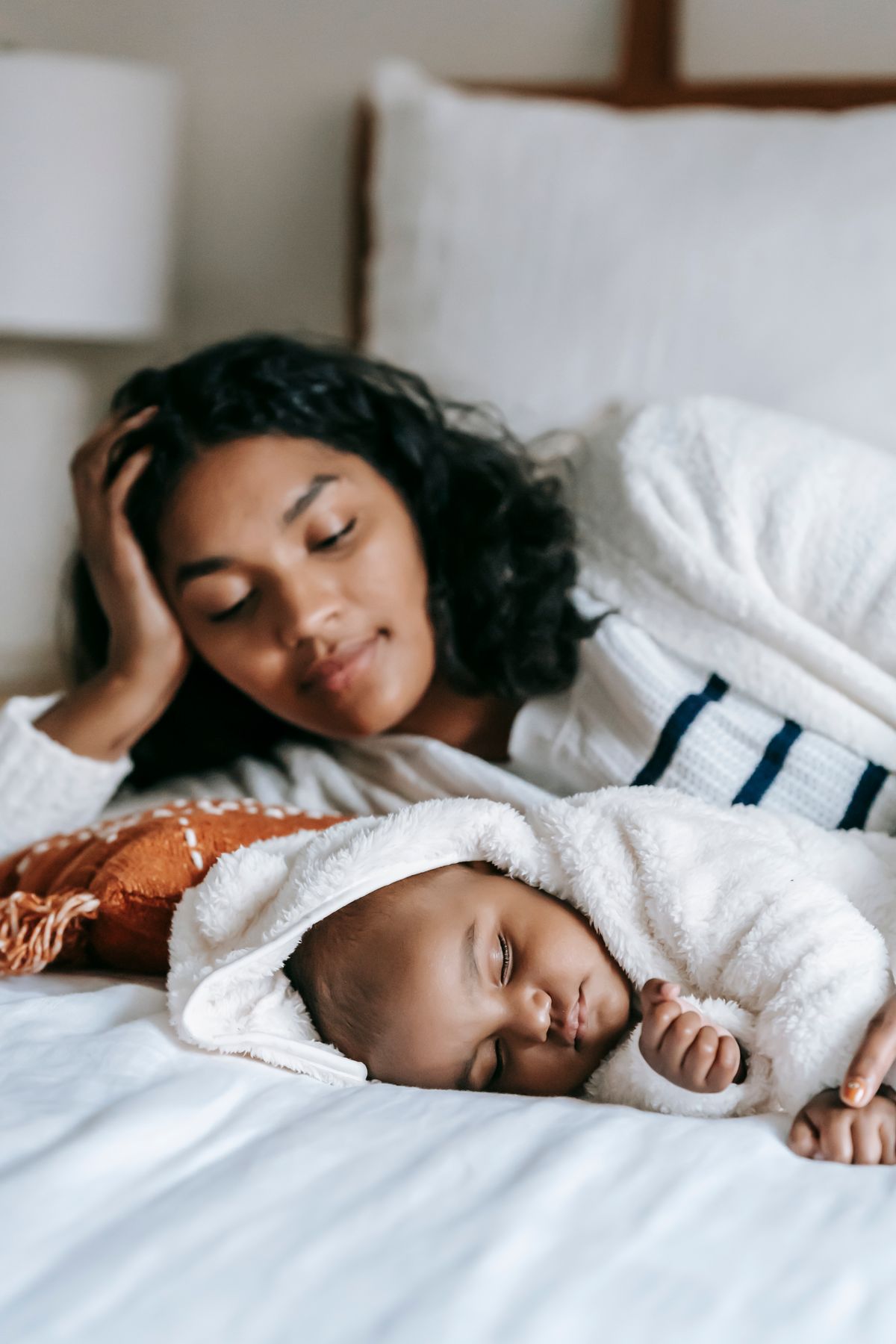 A mother lying on a bed, resting her head on her hand and watching her baby sleep beside her