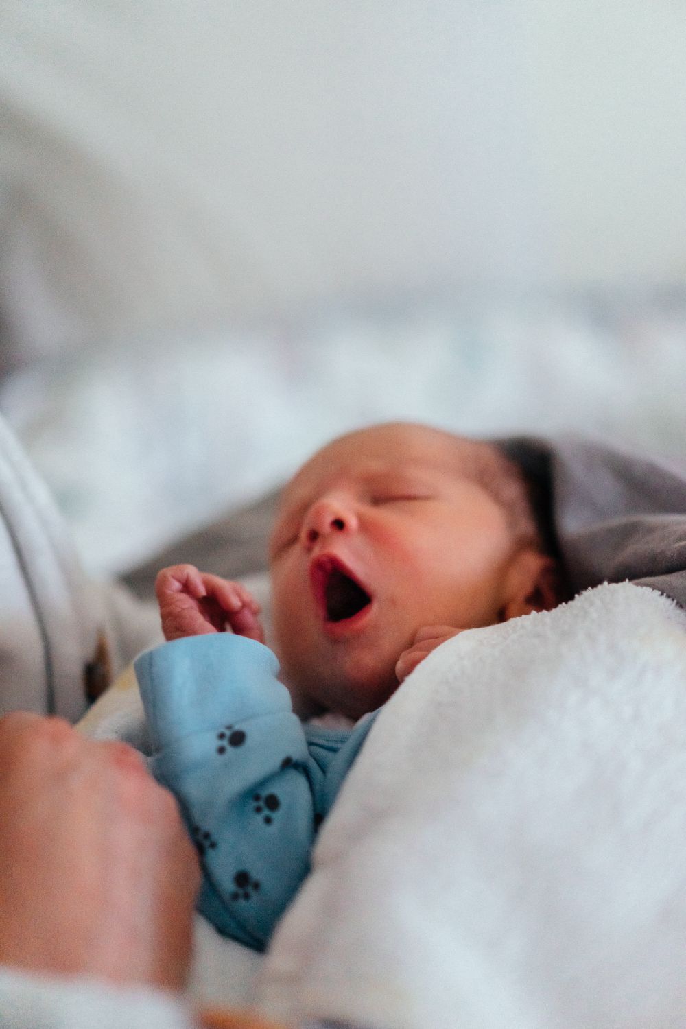 A close-up of an alert newborn bringing a hand to their mouth, a classic early hunger cue