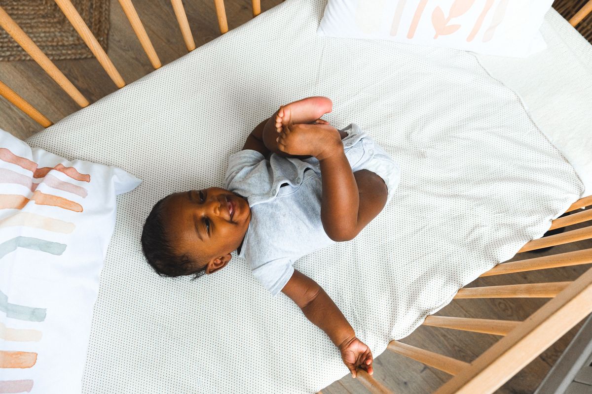 Overhead view of a baby lying in a wooden crib on a dotted sheet, seen from the angle a nursery camera would use