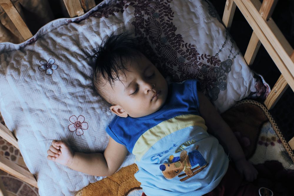 A toddler sleeping in a crib with a soft blanket in a calm, dim room