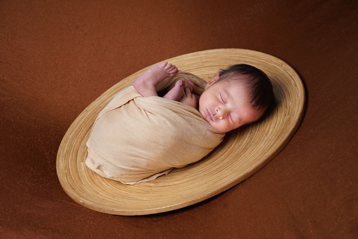 Swaddled newborn sleeping peacefully in a woven bowl