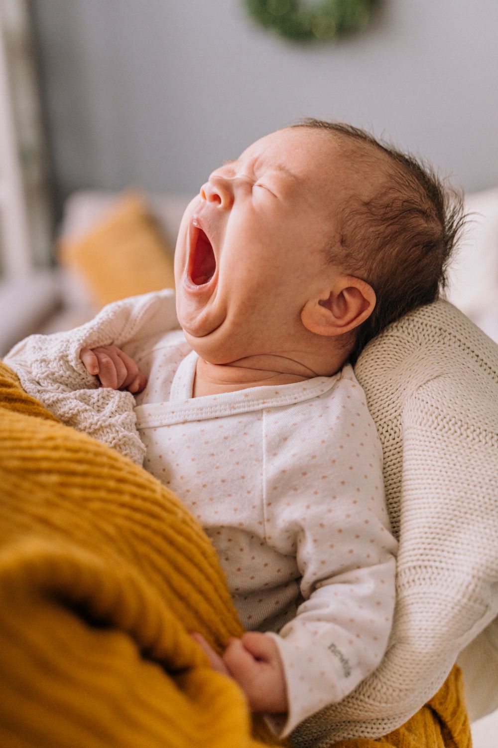 Fussy wide-eyed baby resisting sleep in a parent's arms in a dim room