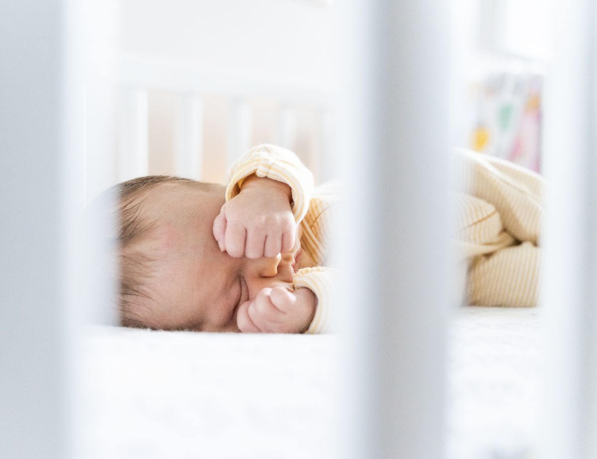 Peaceful baby sleeping on their back in a dark, uncluttered crib at night