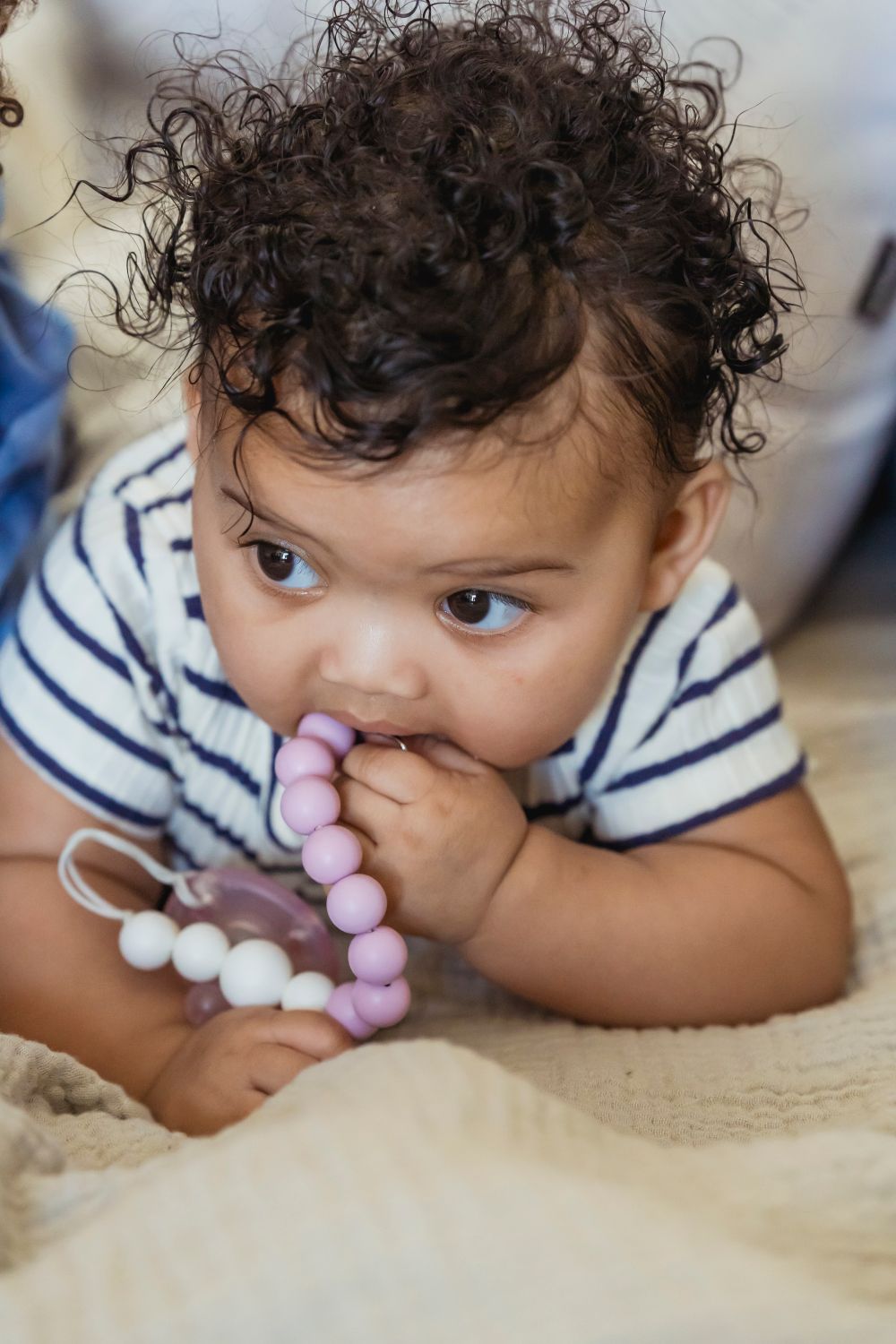 Baby chewing on a teether while lying awake in a crib, drooling and rubbing their gums